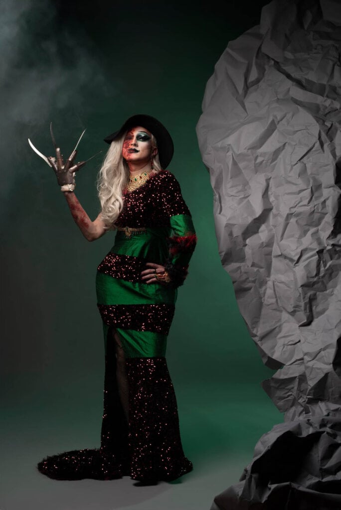 Frau mit weitem Kleid, Hut, gefärbten Kontaktlinsen und Krallenhand in expressiver Pose