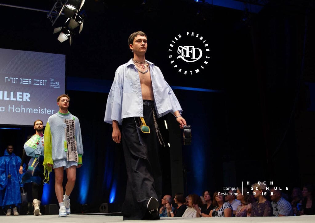 Gruppe von Männermodels auf dem Laufsteg, Frontmodel im offenen Hemd und Hosenrock